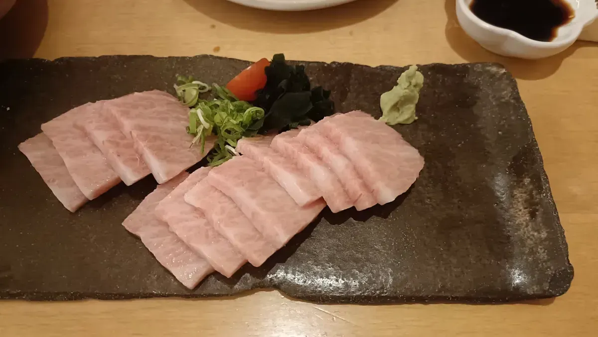Rebanadas de sashimi de atún en un plato rectangular con wasabi, guarnición y salsa de soja de fondo.