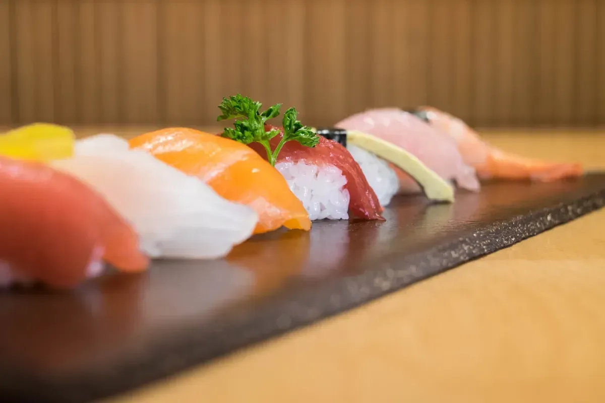 Nigiri de sushi en plato negro: atún, pescado blanco, salmón, atún rojo, pescado con guarnición y camarones.