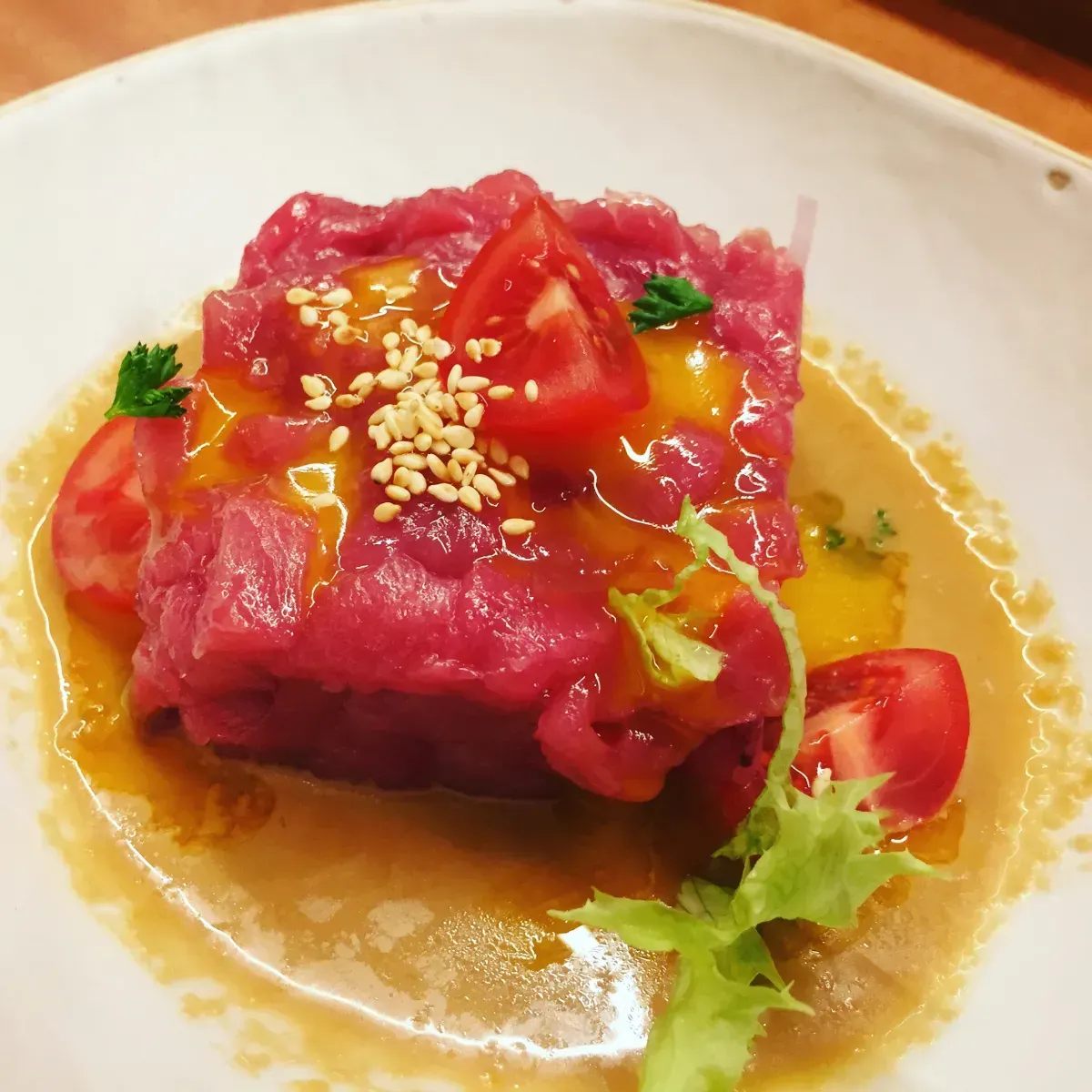 Plato de carne cruda con salsa, tomates cherry y semillas de sésamo en un recipiente blanco.
