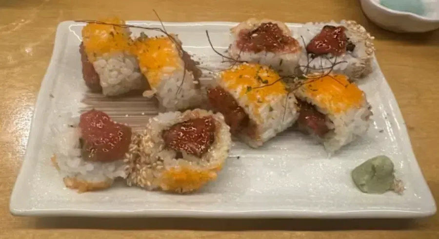 Rollos de sushi en un plato blanco con wasabi. Algunos rollitos llevan salsa amarilla y semillas de sésamo.