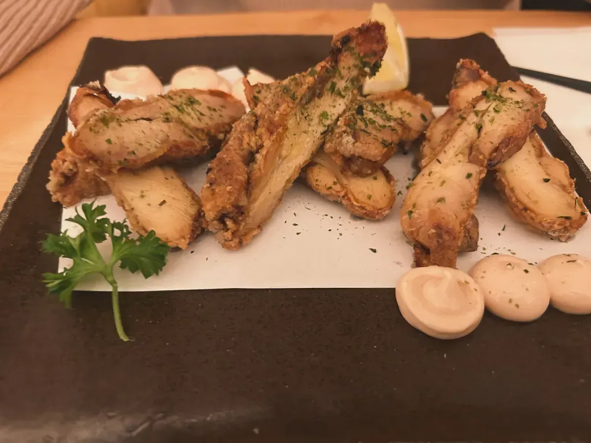 Hongos ostra fritos en un plato negro con papel blanco, pequeñas cucharadas de salsa y guarnición de perejil.