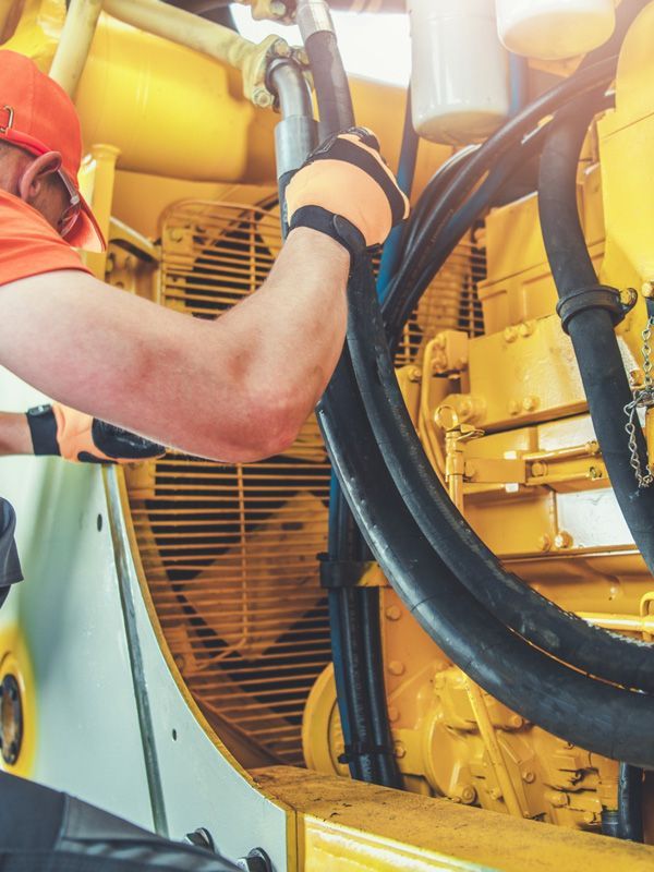Mecánico trabajando con maquinaria amarilla, vistiendo casco y guantes naranjas.