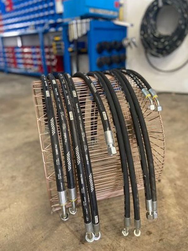 Mangueras hidráulicas negras en una cesta de alambre de color cobre, entorno de taller.