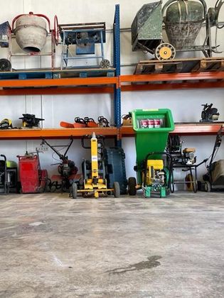 Sala de almacenamiento de equipos con estanterías de maquinaria, incluidas hormigoneras y una trituradora de madera.