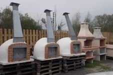 Tres hornos de pizza exteriores con chimeneas metálicas y dos chimeneas de ladrillo dispuestas sobre palés de madera en un patio.