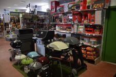En el interior de una tienda se exhiben diversas parrillas de carbón y de gas, con accesorios para asar en cajas colocados en estantes de la pared.