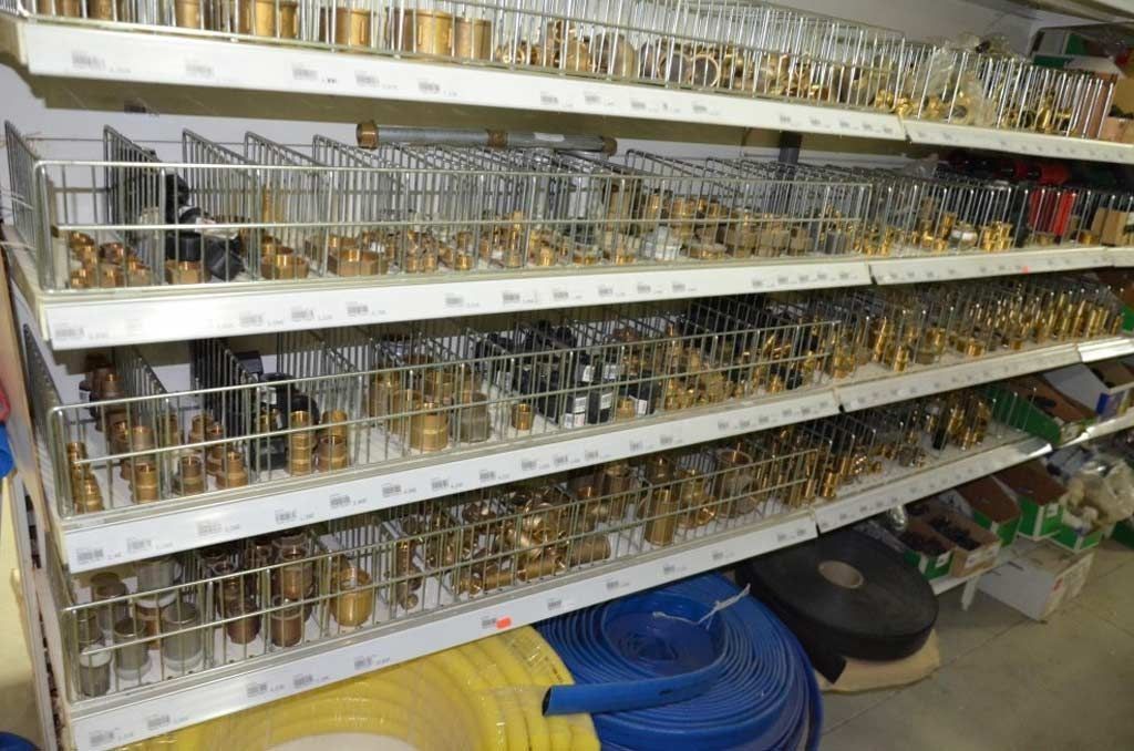 Estanterías de una ferretería repletas de diversos accesorios de fontanería de latón y segmentos de tubería en cestas de alambre.