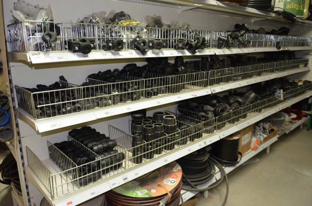 Estanterías de una ferretería repletas de diversos accesorios de fontanería negros y mangueras enrolladas.