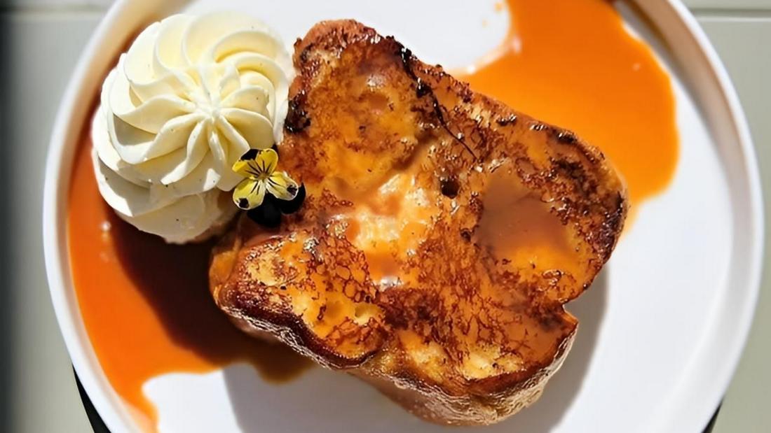 Pain perdu garni de crème fouettée et d'une petite fleur, servi sur une assiette blanche avec une sauce à l'orange