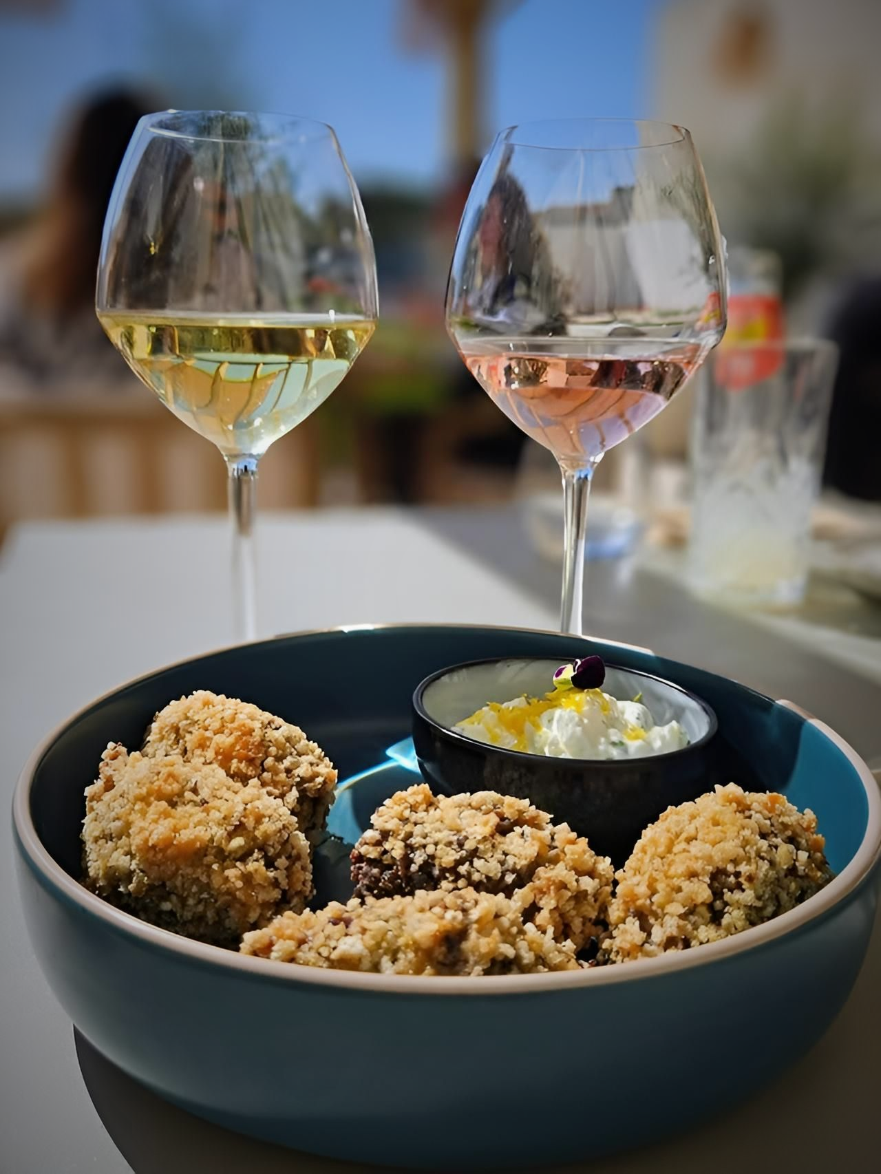 Des verres à vin et un bol de mignardises sur une table à l'extérieur, avec un petit bol de crème derrière.