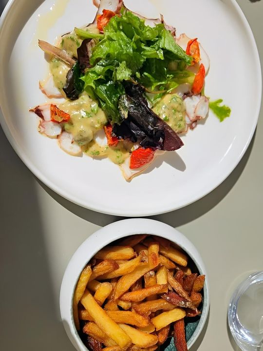 Vue de dessus d'une salade et de frites sur une table blanche, avec un verre à côté.