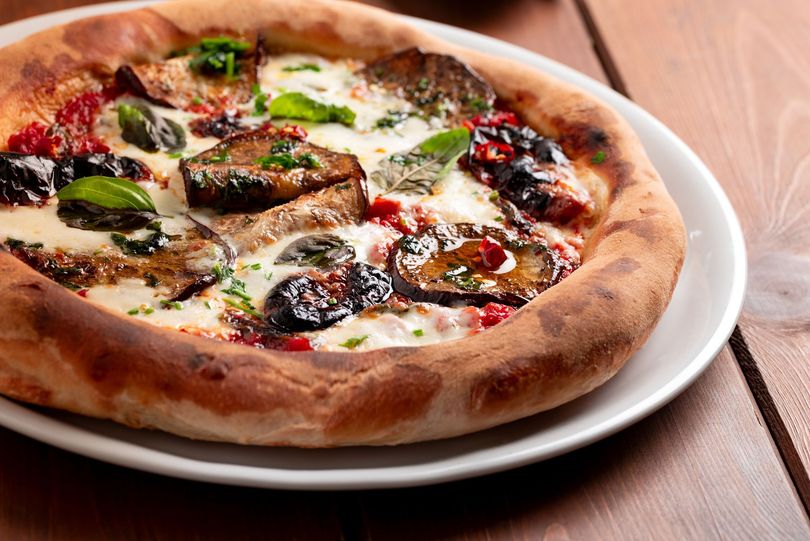 Gros plan d'une pizza aux légumes avec du basilic et du fromage fondu sur une assiette blanche