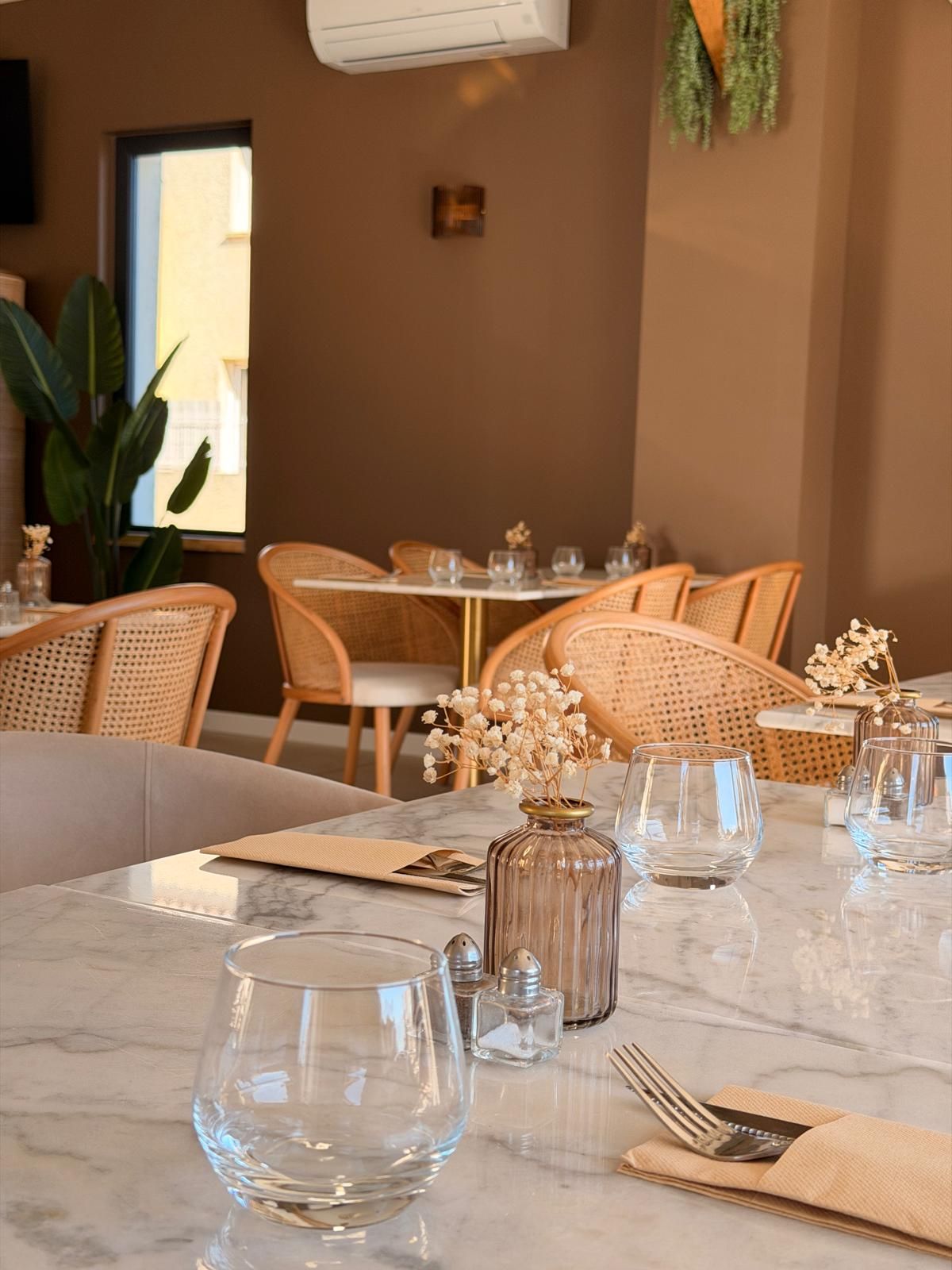 Salle à manger chaleureuse d'un restaurant avec chaises en osier, tables dressées et vase de fleurs blanches.