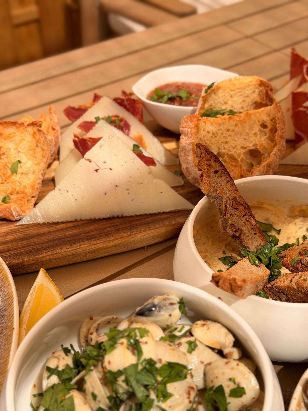 Assortiment d'amuse-gueules sur une table en bois, comprenant des bruschettas, du fromage et un plat crémeux aux champignons.