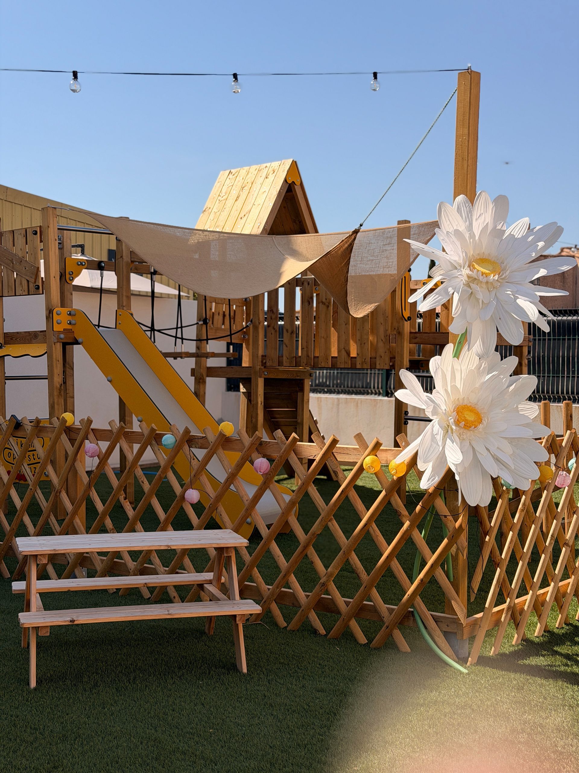 Cour arrière ensoleillée avec clôture en bois, banc et grandes fleurs blanches décoratives au premier plan