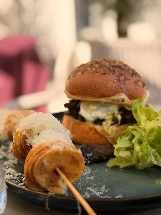 Burger avec salade et brochette grillée sur une assiette foncée, gros plan sur une table