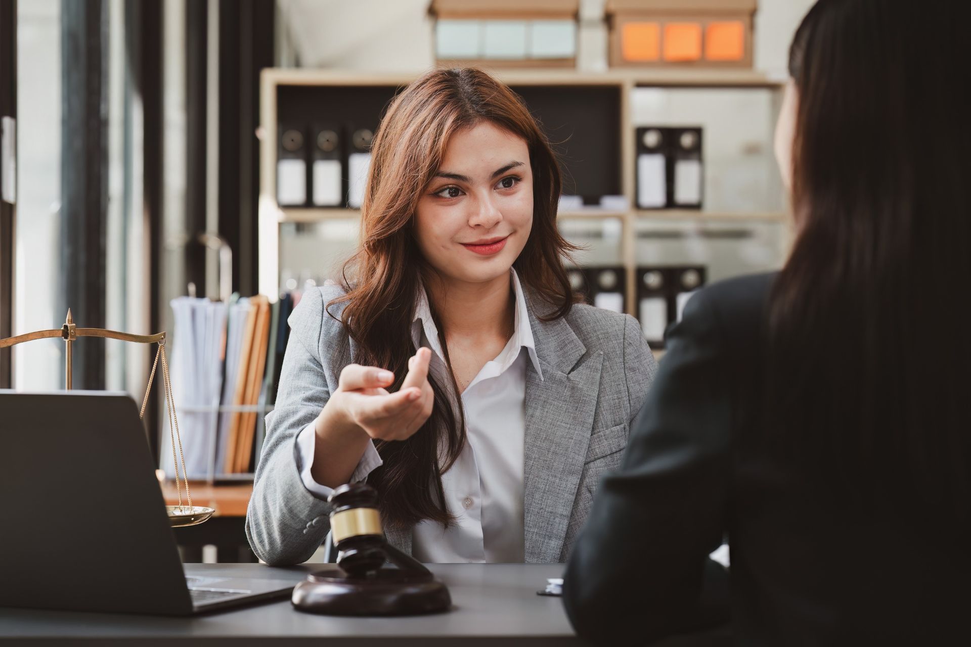 Una mujer está sentada en un escritorio hablando con otra mujer.