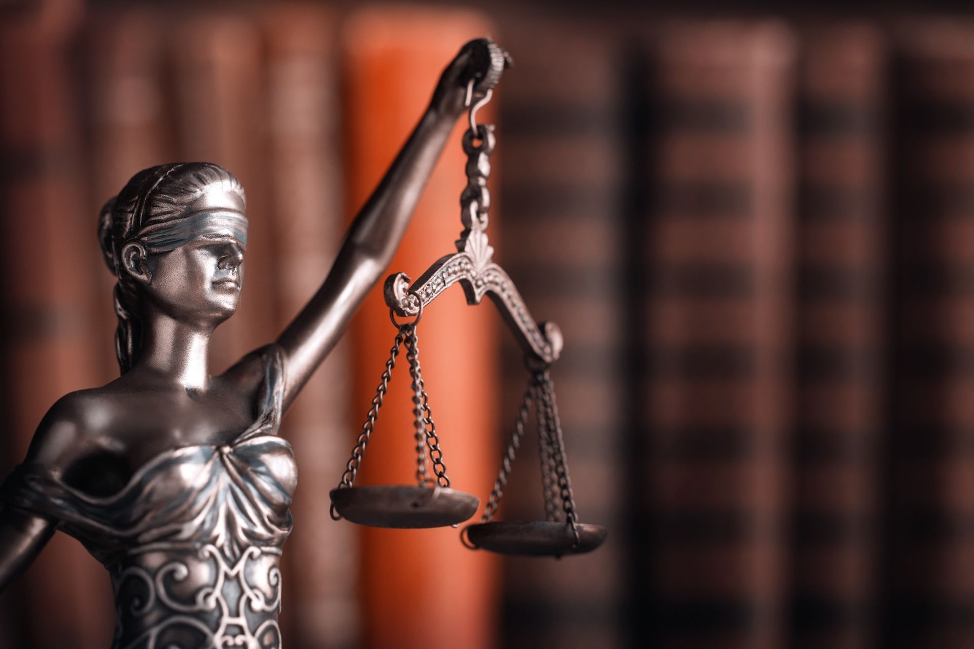 Una estatua de la Dama de la Justicia sosteniendo una balanza frente a una estantería.
