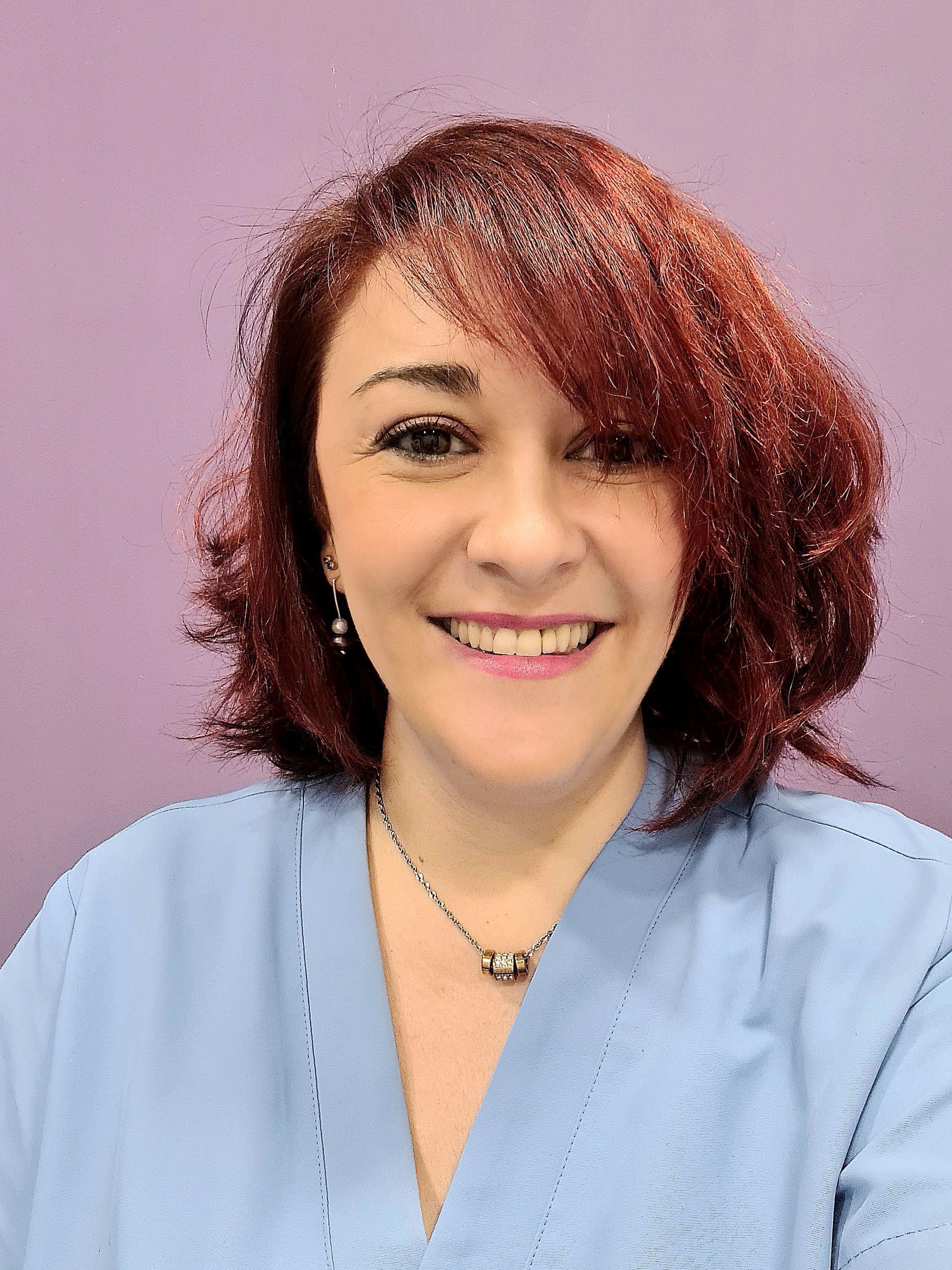 Una mujer con camisa azul y pendientes sonríe a la cámara.