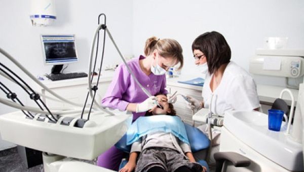 Un niño pequeño está siendo examinado por dos dentistas.