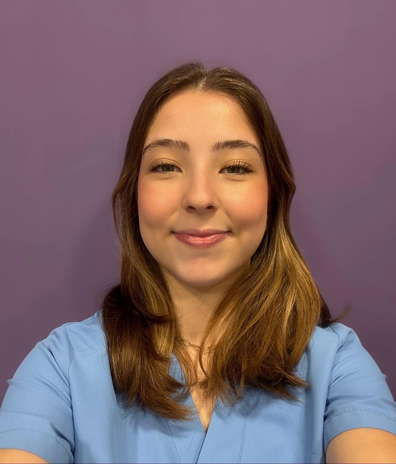Una mujer con una camisa azul está parada frente a una pared violeta.