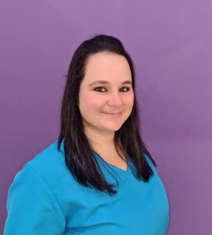 Una mujer con una camisa azul está parada frente a una pared violeta.