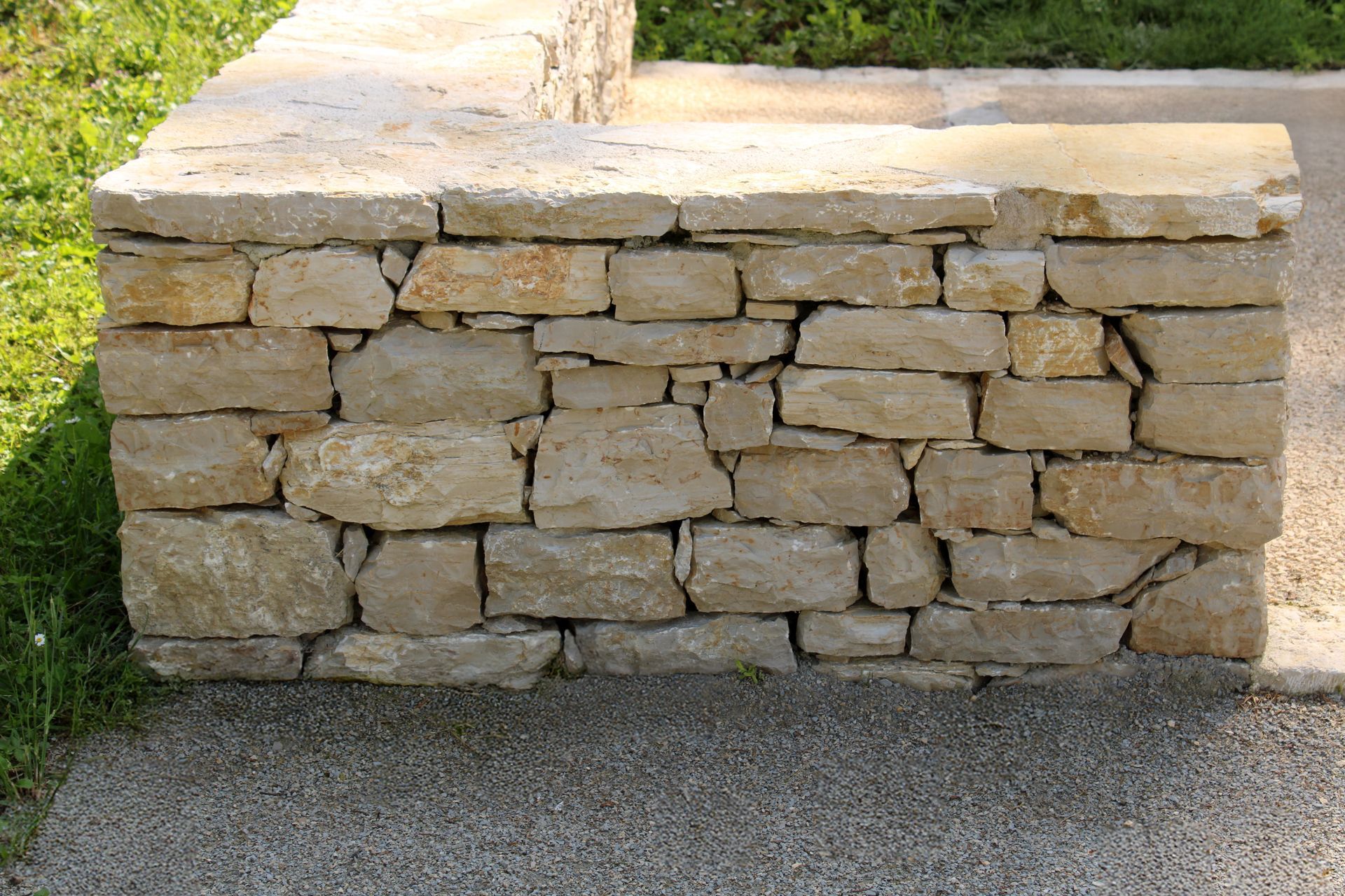Mur de soutènement en pierre bordant un chemin de gravier.