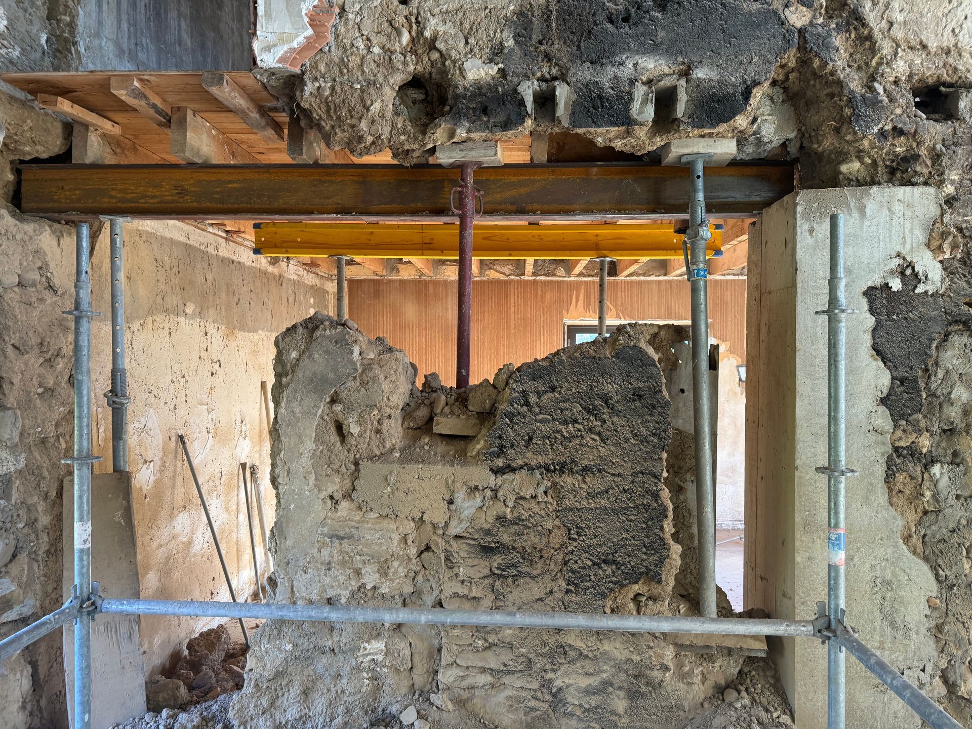 Échafaudages à l'intérieur d'un bâtiment endommagé, encadrement d'un mur effondré avec des décombres apparents.