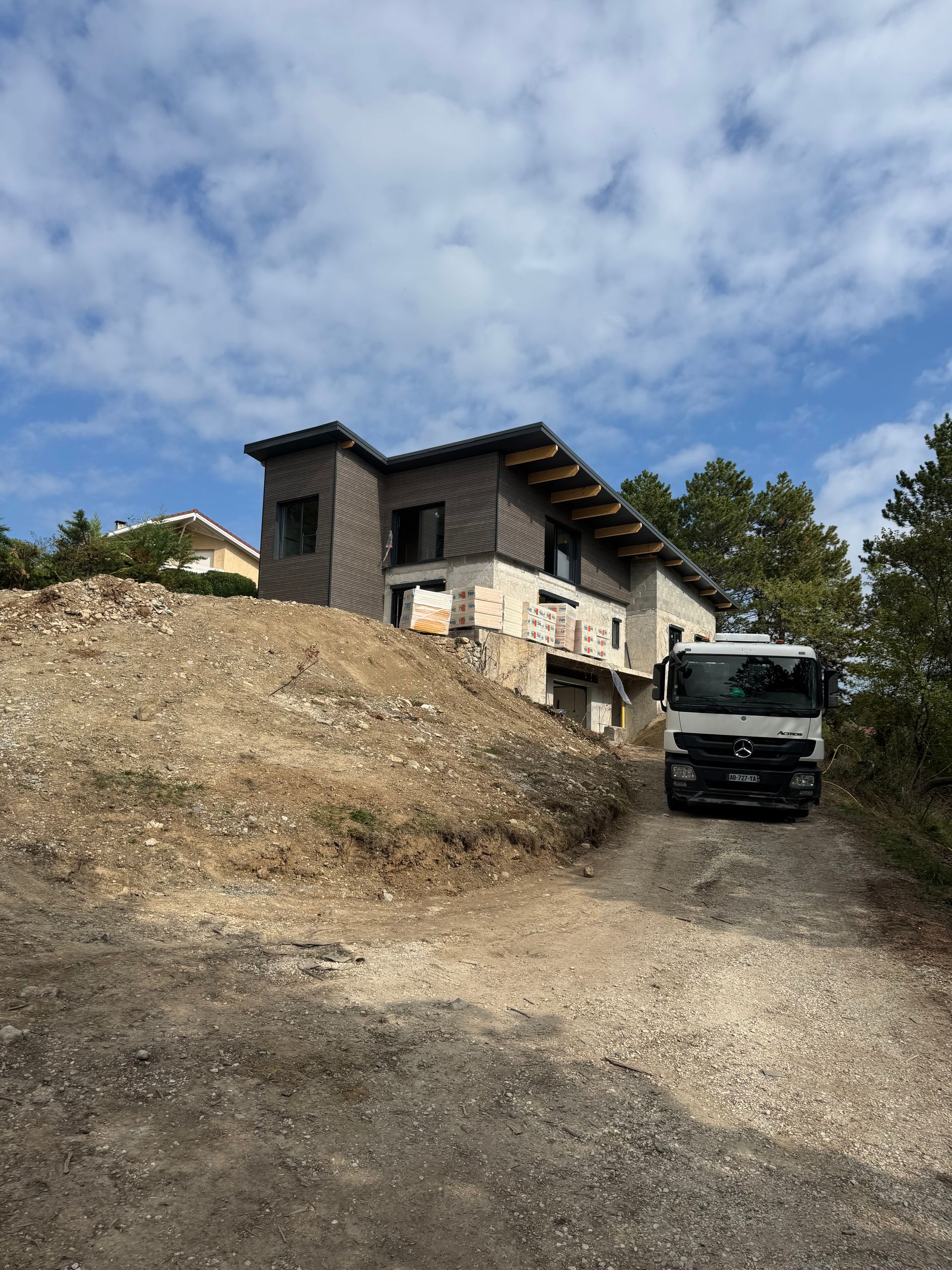 Un camion de chantier blanc est garé sur un chemin de gravier devant une maison moderne en construction.