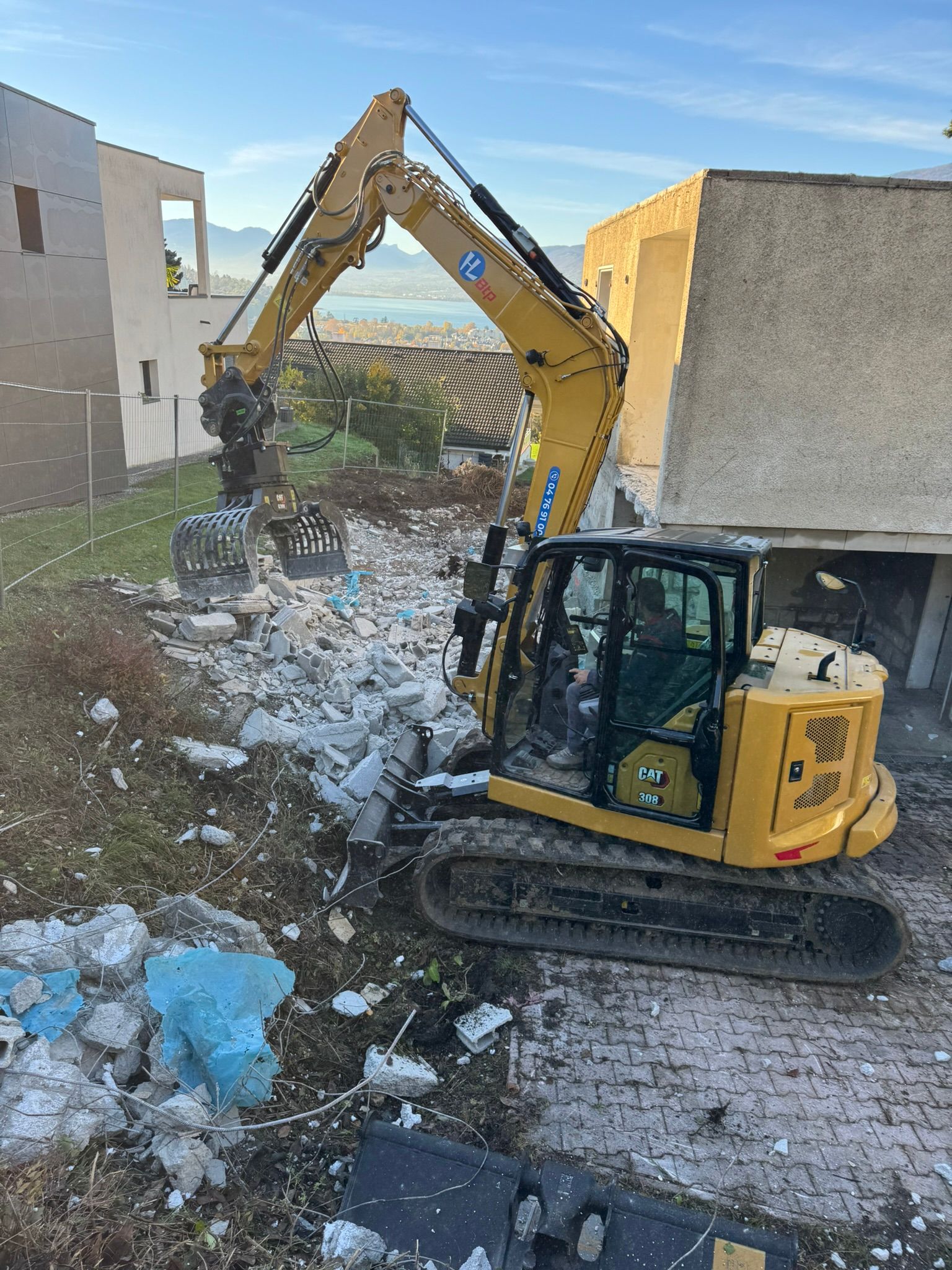 Une petite pelleteuse jaune travaille à l'intérieur d'un espace en béton, dégageant les décombres d'un sol démoli.