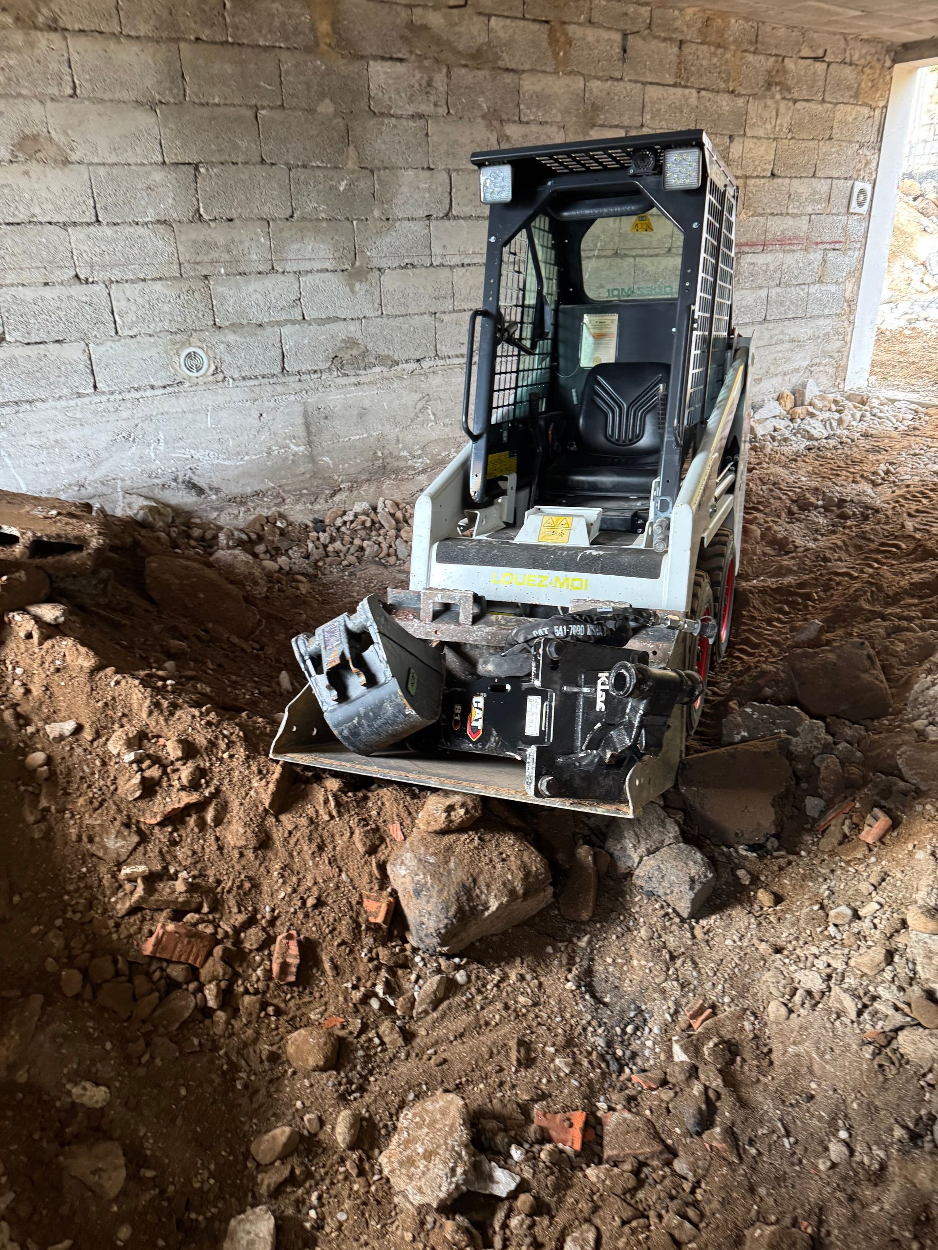 Une chargeuse compacte Bobcat blanche est garée sur un chantier composé de terre.