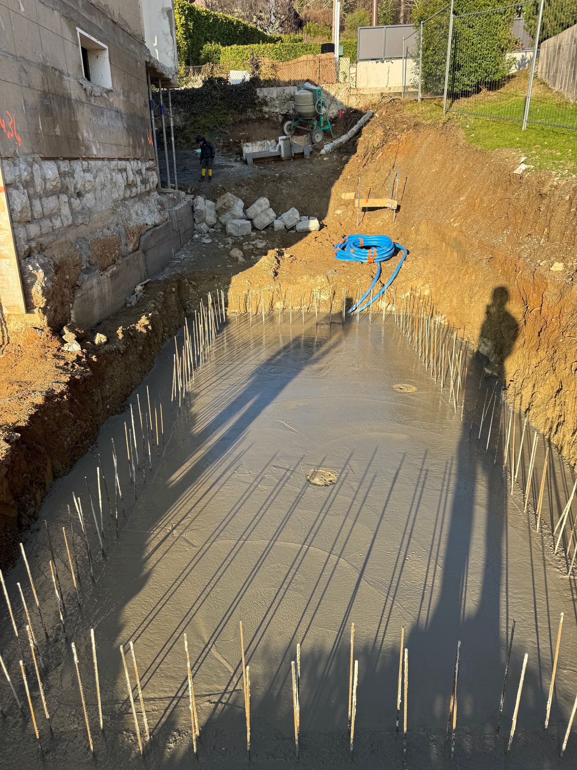Une fondation rectangulaire excavée, avec des barres d'armature verticales dépassant du béton frais.