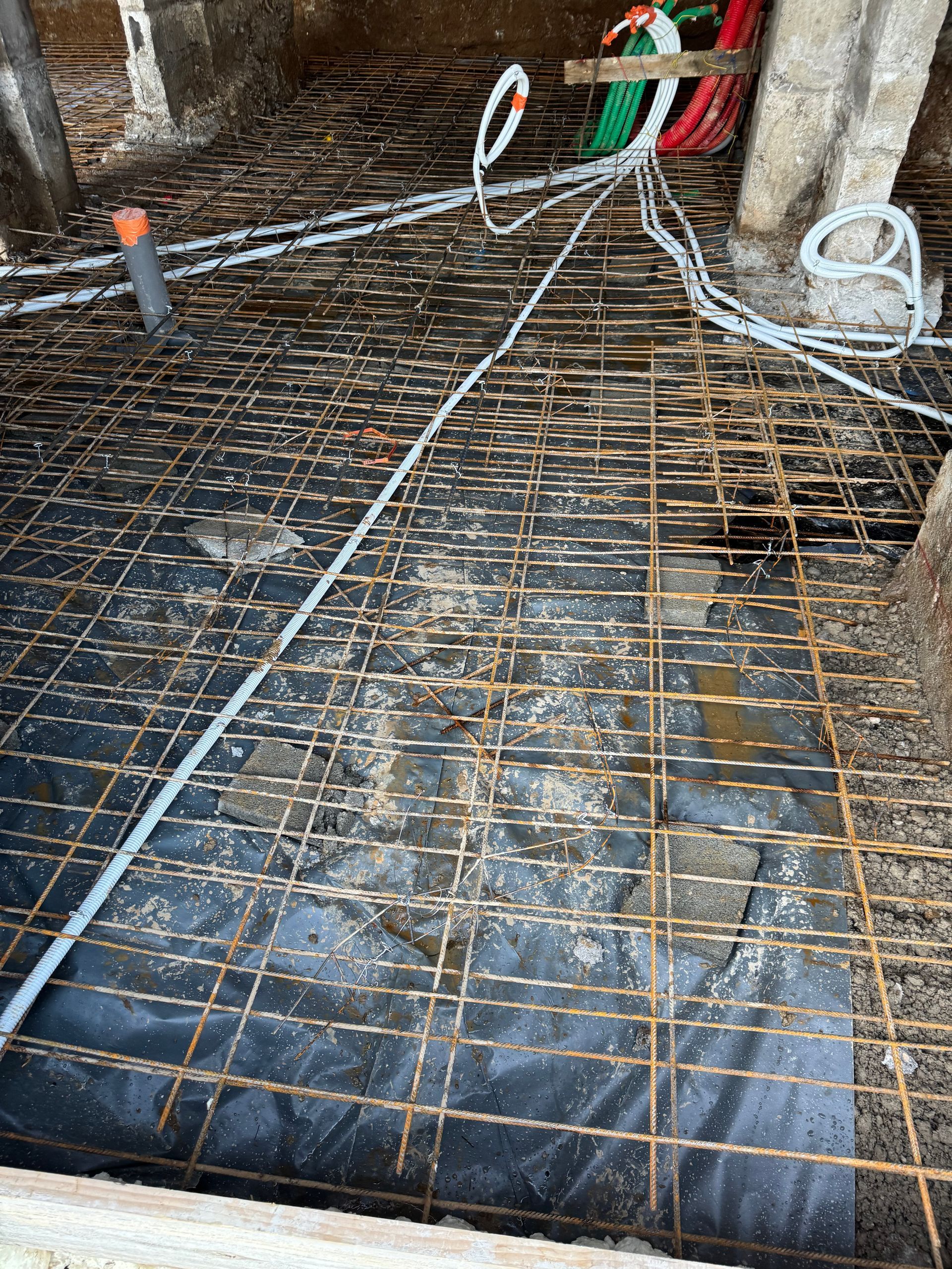 Treillis métallique recouvrant une membrane d'étanchéité noire sur un sol en construction, à proximité de câbles enroulés.