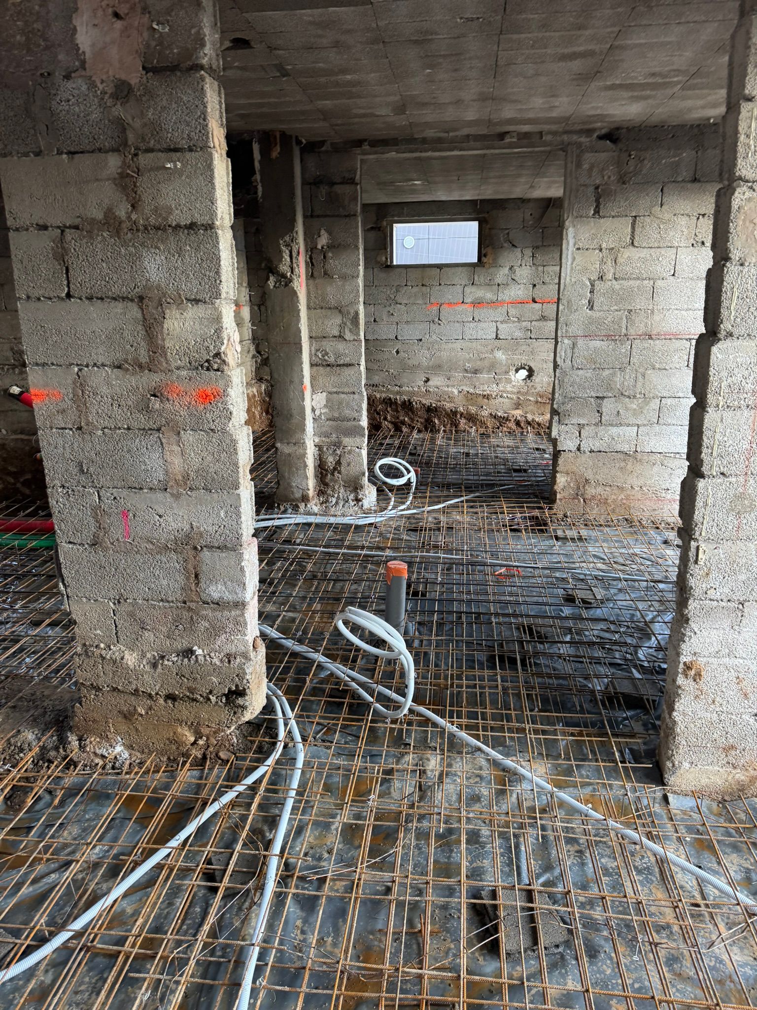 Un chantier de construction avec un ouvrier debout près d'une tranchée contenant des tuyaux de service.
