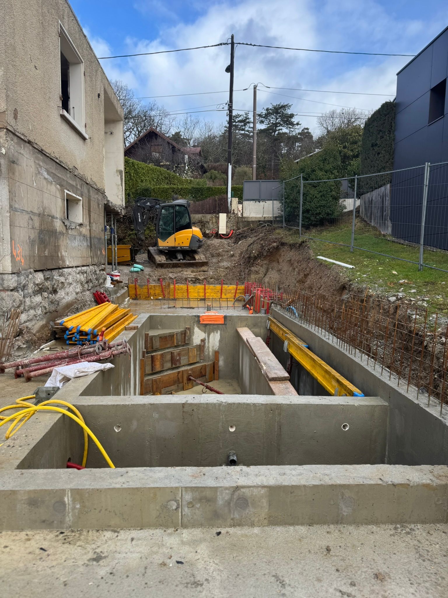 Une maison en construction, avec des échafaudages présentant des murs en béton brut et des portes ouvertes.