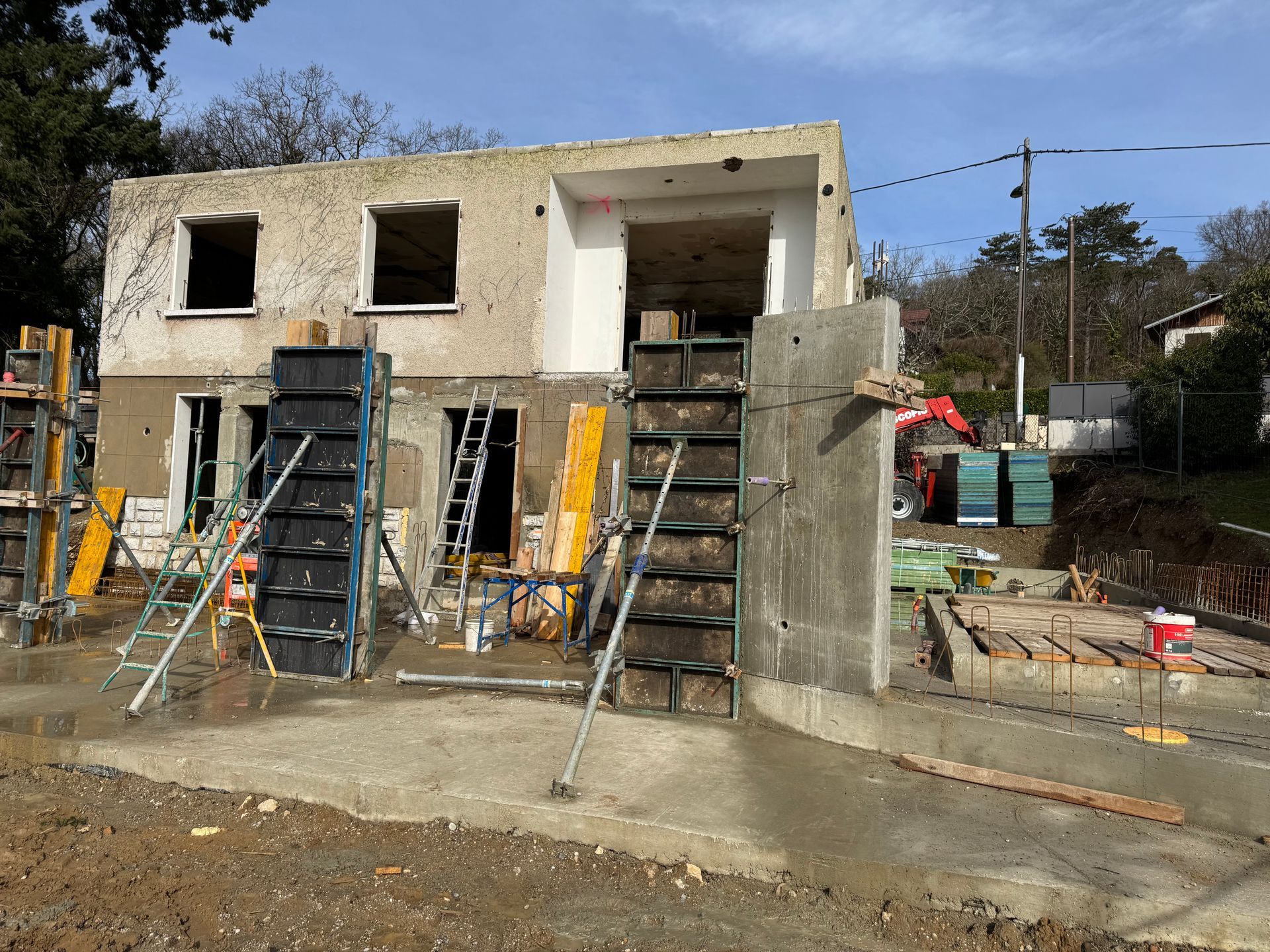 Maison à deux étages en construction avec échelles, échafaudages et murs en béton inachevés