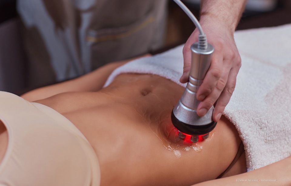 Therapeut verwendet während einer Spa-Behandlung ein handgeführtes Rotlichtgerät am unteren Rücken einer Person.
