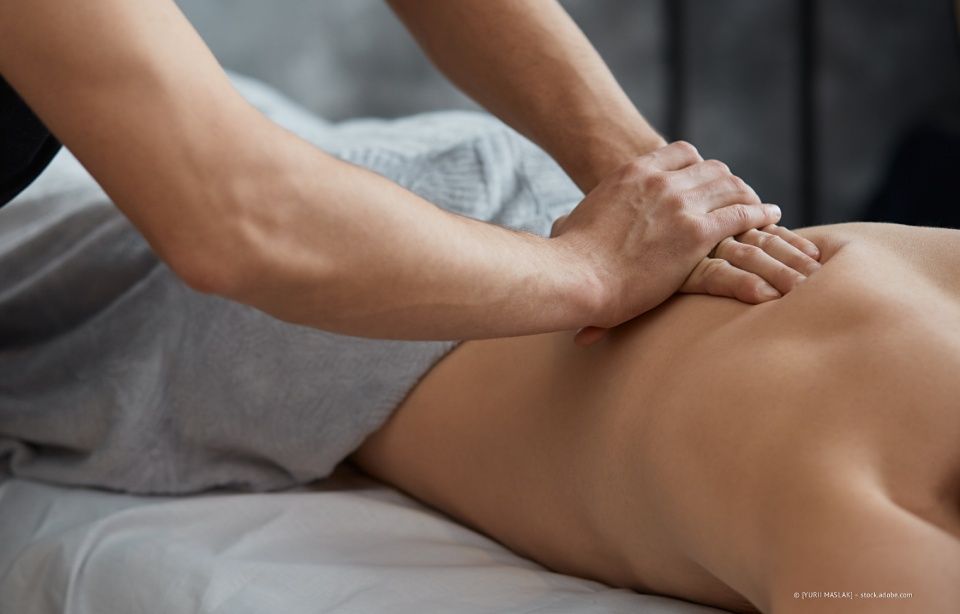 Ein Massagetherapeut drückt den unteren Rücken eines Klienten auf eine Behandlungsliege.
