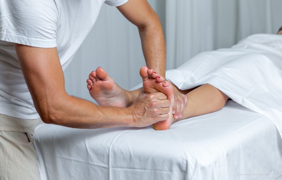 Eine Therapeutin massiert die Füße eines Kunden auf einer Behandlungsliege in einem spa-ähnlichen Raum.