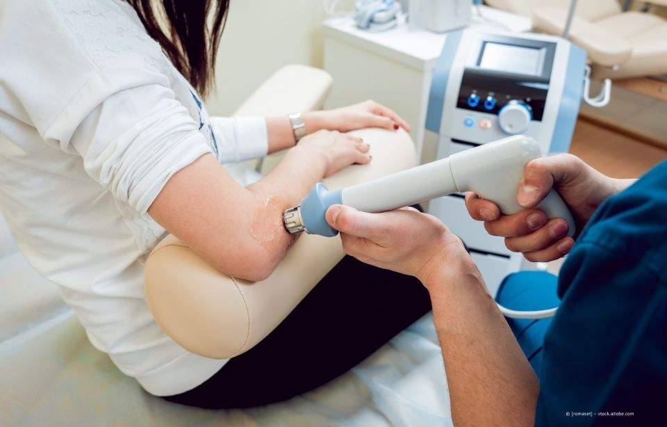 Klinische Behandlung mit einem Handgerät am Arm eines sitzenden Patienten