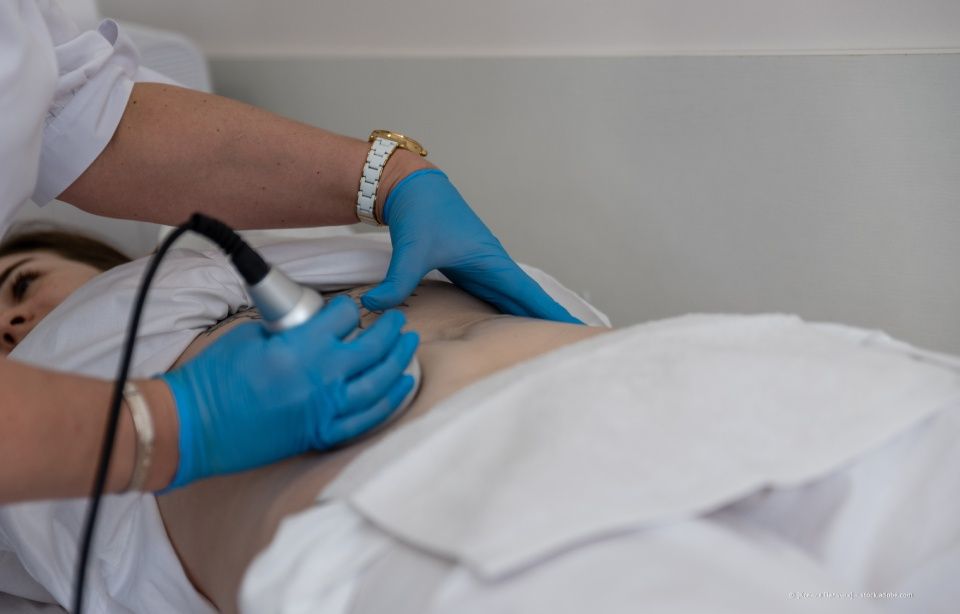 Ein mit Handschuhen bekleideter Arzt führt eine Ultraschalluntersuchung an einem Patienten durch, der auf einer Behandlungsliege liegt.