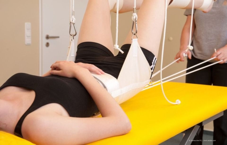 Ein Physiotherapeut dehnt das Bein eines Patienten mit einem blauen Widerstandsband auf einer Behandlungsliege.