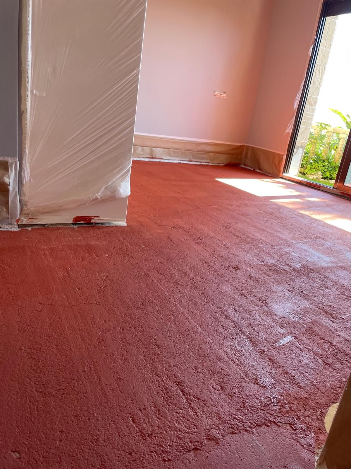 Piso texturizado de color rojo, pasillo con paredes rojas, molduras blancas y un toque de vegetación.