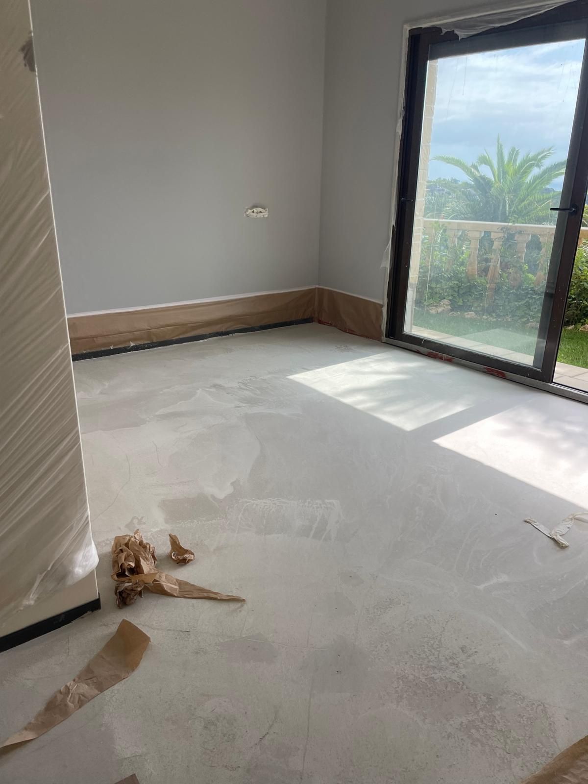 Habitación vacía con paredes de color gris claro, ventana grande, suelo de color claro y molduras de madera.