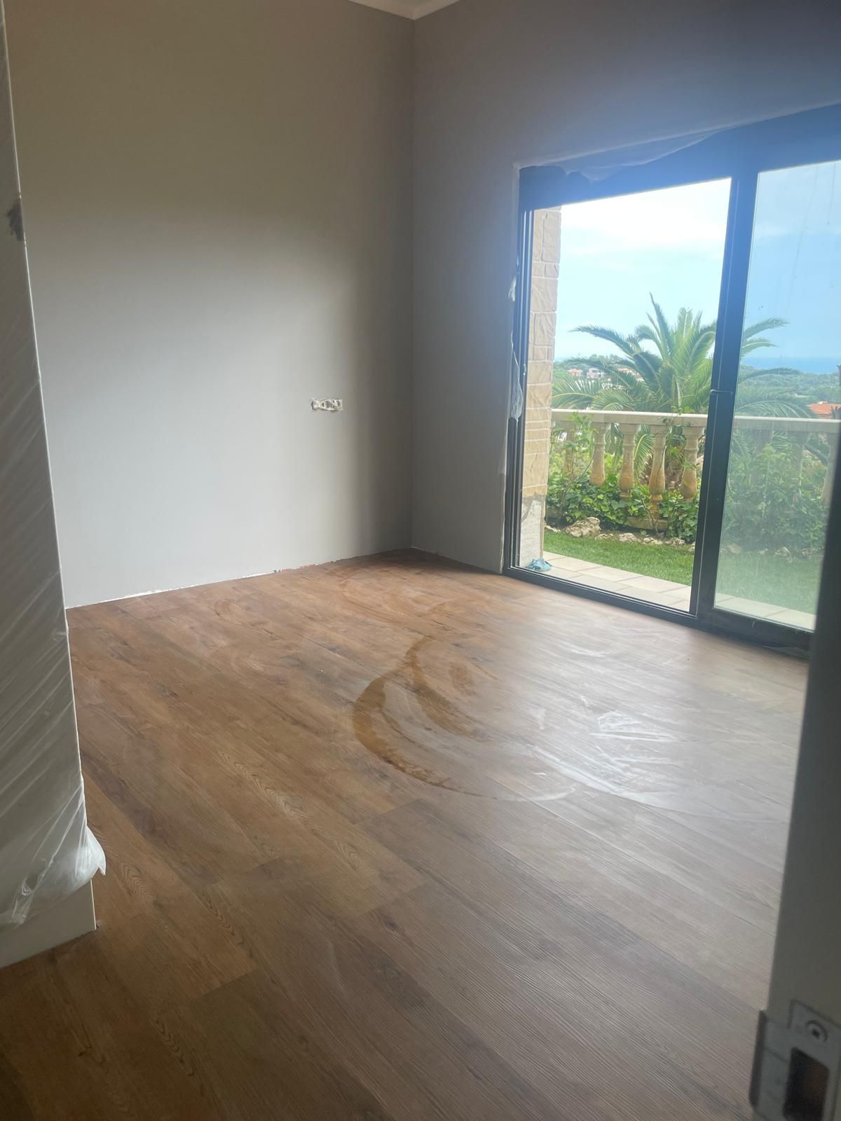 Habitación vacía con piso de madera, paredes grises y una gran puerta corrediza de vidrio que se abre a un jardín.