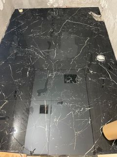 Piso de baldosas con apariencia de mármol negro en un baño, con un panel de acceso cuadrado.