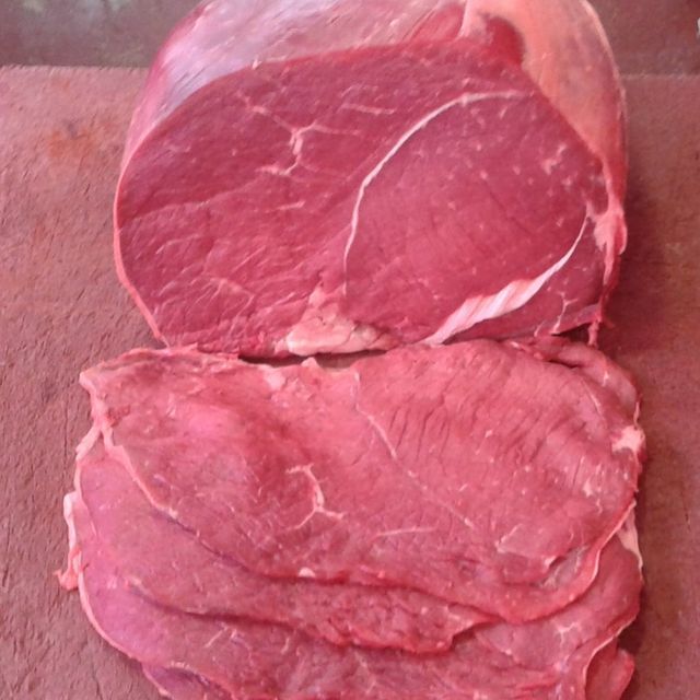 Un gran trozo de carne cruda se encuentra sobre una tabla de cortar.