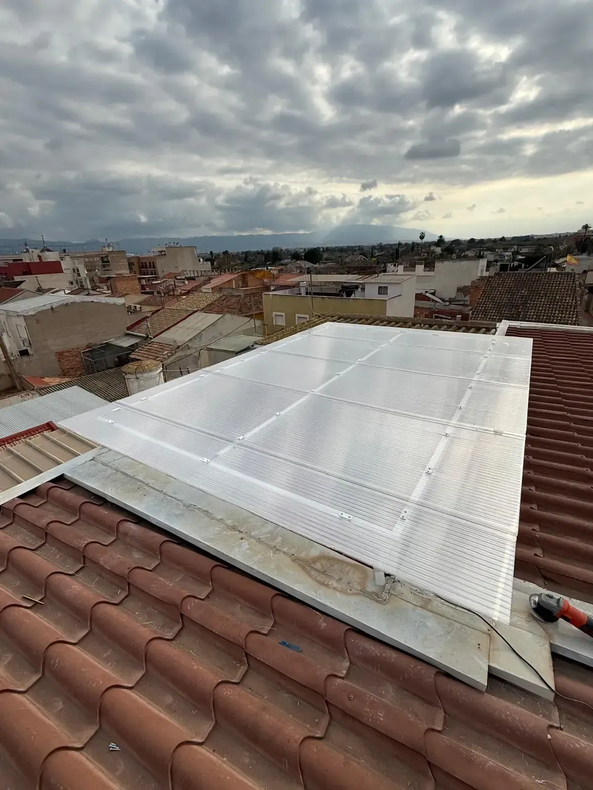 Azotea con un gran conjunto de paneles solares blancos sobre un tejado de tejas rojas bajo un cielo nublado.