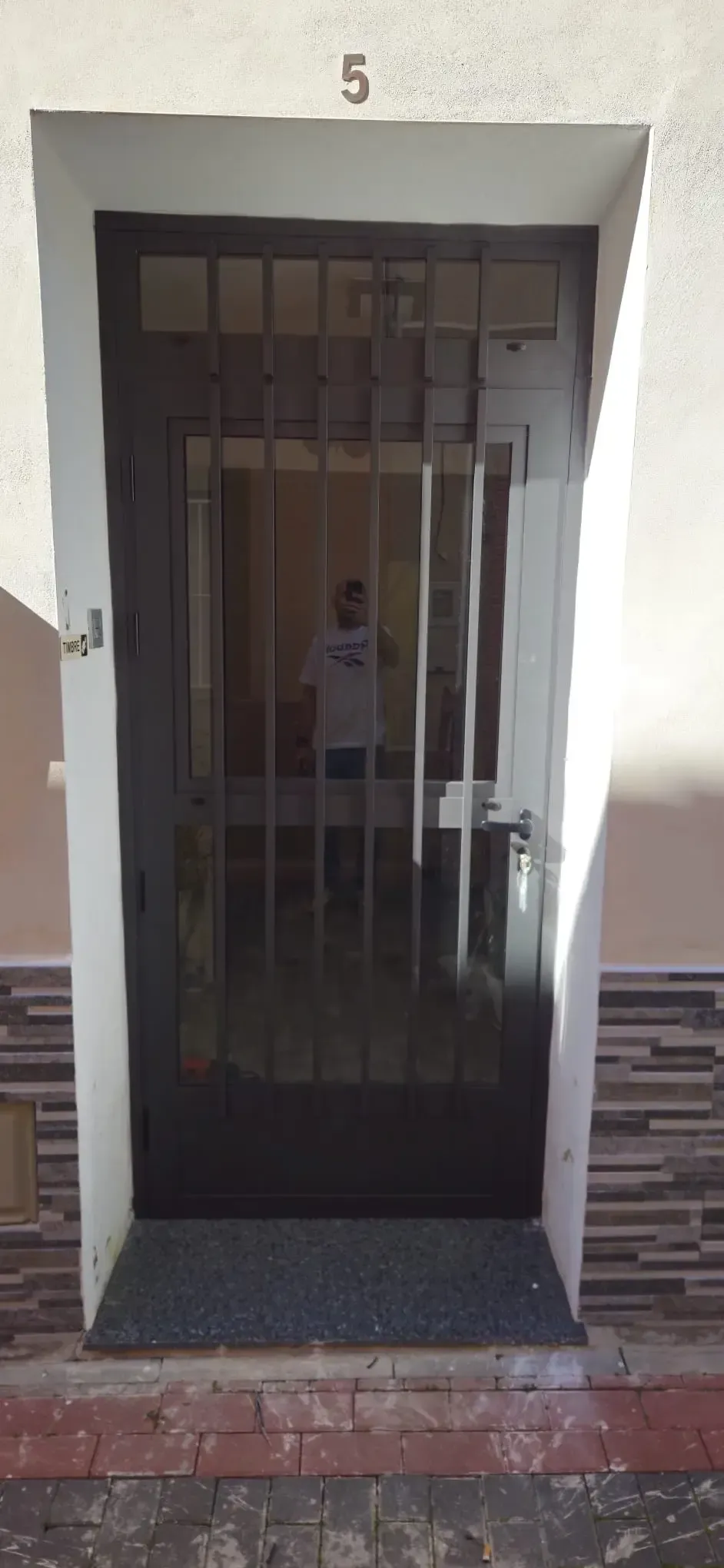 Entrada estrecha con verja metálica y puerta negra, número 5, en la entrada de un edificio.