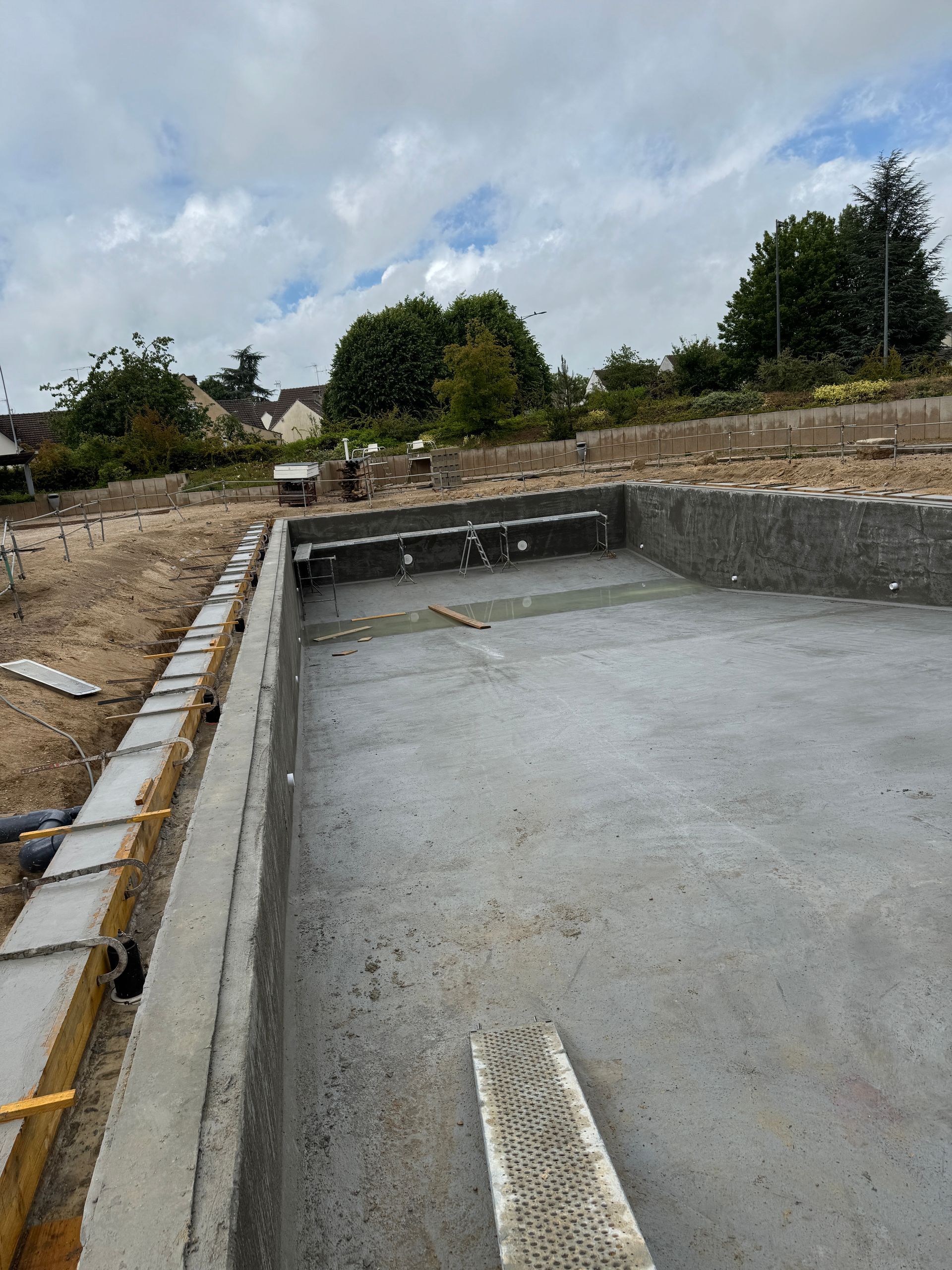 Piscine en béton en construction à l'extérieur avec murs en ciment gris et ciel nuageux.